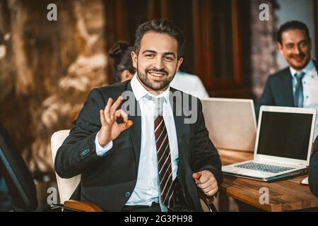 Il Business Person intelligente mostra OK Sign-posing presso la fotocamera Foto Stock