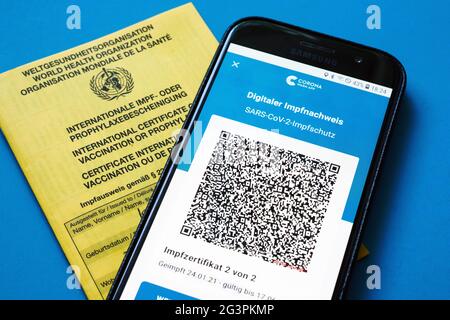 QR-Code, das digitale Impfzertifikat in der Corona WARN-App auf einem smartphone bestätigt eine abgeschlossenen Impfung gegen Covid-19. Liegt auf der gelben Internationalen Impfbescheinigung, Impfpass. ACHTUNG! QR-Code und persönliche Angaben sind unkenntlich gemacht! Foto Stock