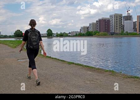 Vista posteriore della donna che cammina lungo il sentiero nella riserva naturale Walthamstow Wetlands e nuovi edifici in costruzione a Londra N17 KATHY DEWITT Foto Stock