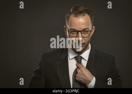 Sorridente uomo d'affari raddrizza la cravatta. Un banchiere professionale ben vestito guarda con sicurezza e affidabilità la telecamera w Foto Stock