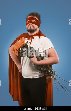 Fiori da super eroe in amore. Uomo che indossa costume rosso supereroe che tiene bouquet di crisantemi per la sua amante donna. Taglia ou Foto Stock