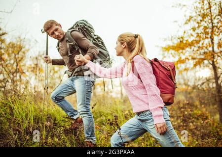 L'uomo aiuta una donna a salire su una collina tenendo la mano della donna e i pali da trekking in altra mano. Concetto di escursionismo. Supporto e assistenza Foto Stock