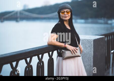 Donna elegante riposa a riva del fiume. Elegante ragazza in piedi sullo sfondo del fiume argine. Concetto di stile di vita. TR Foto Stock