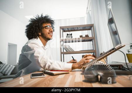 Designer ispirato che lavora al computer con un nuovo progetto. Un giovane uomo freelance lavora su un computer portatile seduto sul posto di lavoro a casa. Vista laterale Foto Stock