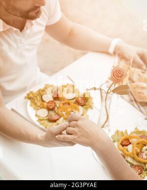 Bella coppia che tiene le mani in spiaggia caffè all'aperto. L'uomo e la donna caucasici sono felici di passare del tempo tra loro. Tenerezza c Foto Stock