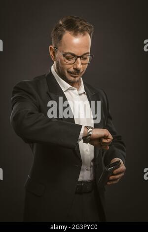 Uomo d'affari controlla il tempo guardando il orologio da polso. Un uomo di mezza età, amichevole, tiene in mano una borsetta in attesa di un amico d'affari Foto Stock