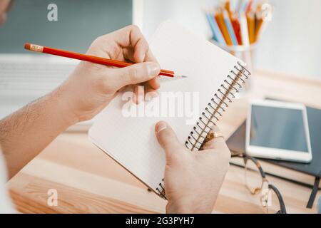 L'uomo d'affari sta progettando una nuova registrazione di avvio in un blocco note. Le mani degli uomini che tengono una matita rossa prendono appunti in un taccuino di carta. B Foto Stock