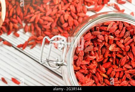 Goji secco aka. Semi di mirtillo all'interno di una bottiglia di vetro, alcuni sparsi su una scrivania di tavole bianche Foto Stock