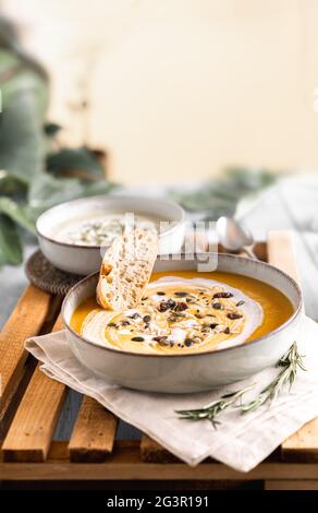 Fotografia alimentare di una zuppa di crema di zucca vegana e pane con fuoco selettivo. Ricetta di verdure. Una purea autunnale di prodotti di stagione su una linguetta di legno Foto Stock