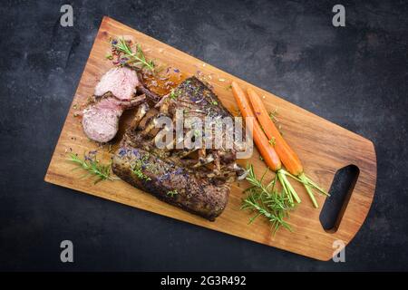 Rack barbecue di agnello con carote ed erbe offerto come vista dall'alto su un tavolo di legno dal design moderno con spazio copia Foto Stock