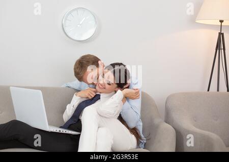 Coppia che riposa sul divano utilizzando il computer portatile. Coppia sposata che ha un po 'di tempo rilassato sul divano a casa. Uomo baciando la sua fidanzata su nec Foto Stock