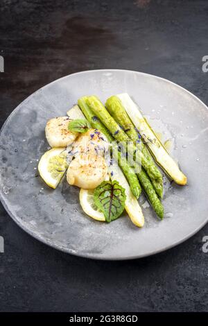 Tradizionali capesante per barbecue con asparagi verdi e bianchi e salsa al burro, da vicino su un piatto dal design moderno Foto Stock