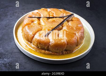 Tatin tradizionale francese con mele e vaniglia offerto da vicino su un piatto dal design moderno con sfondo rustico Foto Stock