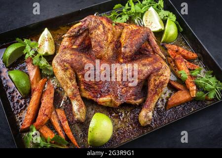Pollo tradizionale al mattone al chcoccato al barbecue con patatine dolci e lime offerti da vicino su un vecchio rusti Foto Stock