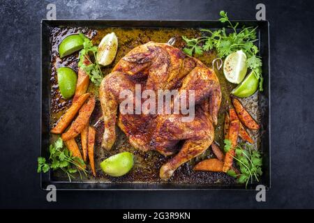 Pollo tradizionale al mattone al choccato al barbecue con patatine dolci e lime offerto come vista dall'alto su un vecchio rusti Foto Stock