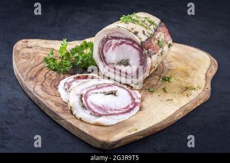 Tradizionale panchetta arrotolata italiana di carne di maiale affettata e come pezzo con erbe offerte da primo piano su una rustica tavola di legno w Foto Stock