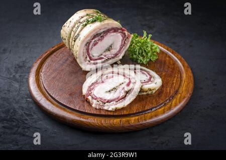 Tradizionale panchetta arrotolata italiana di carne di maiale affettata e come pezzo con erbe offerte da primo piano su una rustica tavola di legno w Foto Stock