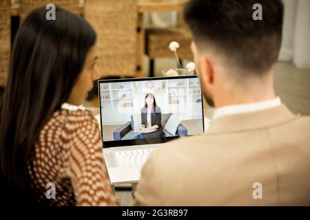 Vista posteriore della giovane coppia sposata moglie e marito discutere questioni e incomprensioni nei rapporti quando hanno consultazione on-line con lo psicologo di famiglia, seduto sul divano nella stanza livinning Foto Stock