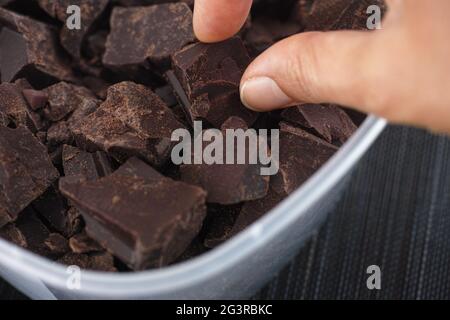 Una donna che prende un pezzo di cioccolato fondente biologico rotto in casa da un contenitore di plastica. Primo piano. Foto Stock