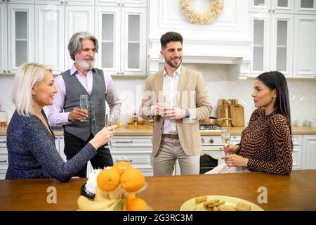 Amorevole giovane figlia fare brindisi mentre festeggia il compleanno del suo padre tenendo un bicchiere di champagne mentre si siede in cucina a casa insieme con madre e marito. Concetto di celebrazione familiare Foto Stock