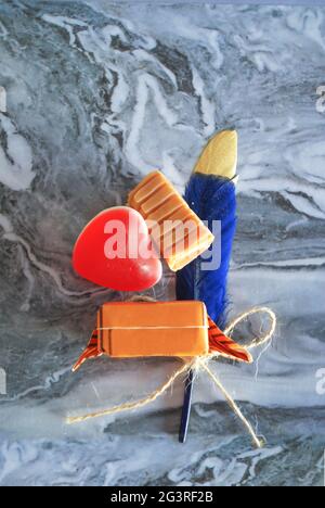 caramelle dolci decorative con piuma blu sfocata su carta ondulata marmorizzata morbida messa a fuoco, tema d'amore che esprime la carta dei sentimenti, gelatina forma del cuore, Foto Stock