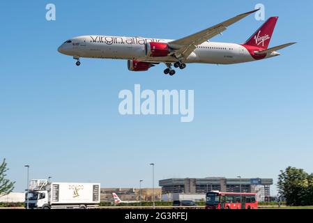 L'aereo jet della Virgin Atlantic Airways G-VOWS in finale atterra all'aeroporto Heathrow di Londra, Regno Unito, su un camion di catering e un autobus di trasporto pubblico Foto Stock