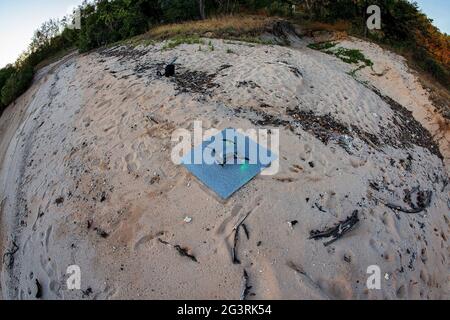 Un drone sulla sua piattaforma di atterraggio sulla sabbia su una spiaggia isolata dopo aver fotografato l'alba, pesce lente occhio Foto Stock