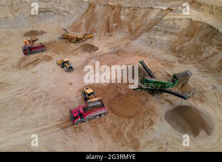 Pala gommata che carica sabbia nel dumper in buca aperta. Vista panoramica della linea di produzione della sabbia dei frantoi a mascelle. Macchinari pesanti per l'estrazione mineraria in cava. Carrello Foto Stock
