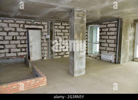 Interno incompiuto dell'appartamento in costruzione con parete in cemento grigio e finestre con doppi vetri in un edificio residenziale a più piani presso un contro Foto Stock