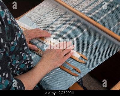 Mani artigiane con due navette sul telaio mano. Tessitura del tessuto a strisce Foto Stock