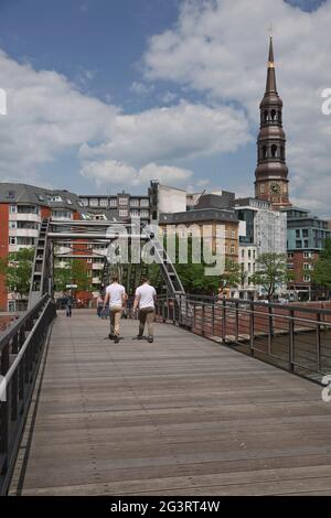 Persone che attraversano il ponte e la vita cittadina ad Amburgo in Germania con la chiesa di Santa Caterina sullo sfondo Foto Stock