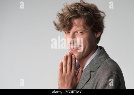 Concetto di richiesta di tipo. Uomo dai capelli ricci simpatico sorridente con palme piegate in preghiera. Primo piano ritratto maschile. Spazio di copia sul lato sinistro Foto Stock