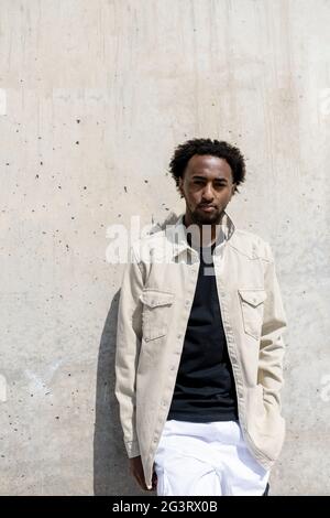 Afro uomo appoggiato su muro di cemento con le mani in tasca Foto Stock