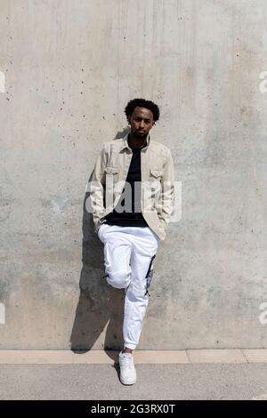 Afro uomo appoggiato su muro di cemento con le mani in tasca Foto Stock