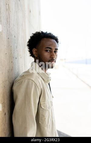 Afro uomo appoggiato su muro di cemento con le mani in tasca Foto Stock