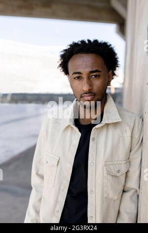 Afro uomo appoggiato su muro di cemento con le mani in tasca Foto Stock