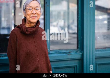 Donna anziana sorridente che indossa occhiali in ambiente urbano Foto Stock