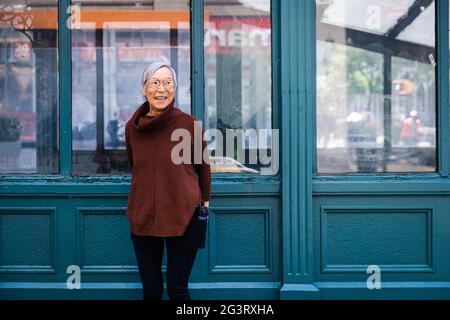 Donna anziana felice che guarda via mentre si sta contro il muro Foto Stock