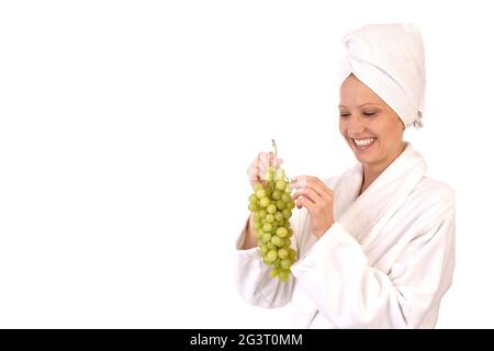 giovane donna in accappatoio bianco che mangia uva Foto Stock