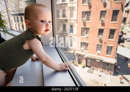 Curiosa bambina felice guardando fuori finestra in città Foto Stock