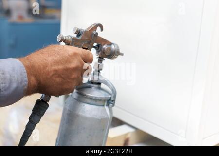 Verniciatura di un prodotto metallico. Primo piano - su di una mano di un pittore con un compressore spray Foto Stock