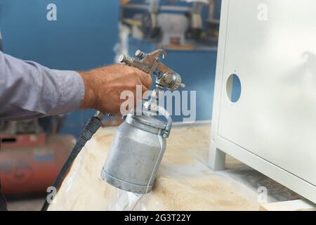 Verniciatura di un prodotto metallico. Primo piano - su di una mano di un pittore con un compressore spray Foto Stock