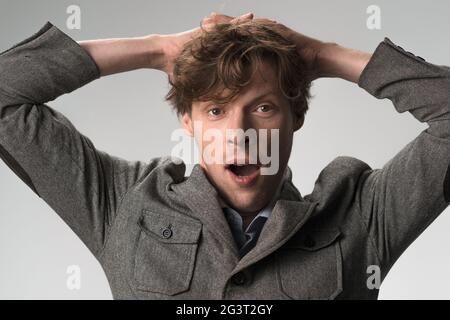 Il giovane annoiato urla tenendo le mani dietro la testa. Primo piano ritratto di maschio in abbigliamento casual isolato su sfondo bianco Foto Stock