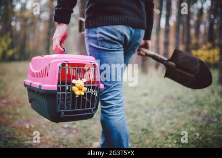 Il tema è la morte dell'animale domestico. Vista posteriore dell'uomo che cammina lungo il sentiero forestale e che porta la pala in una mano per scavare la tomba, e in olio Foto Stock