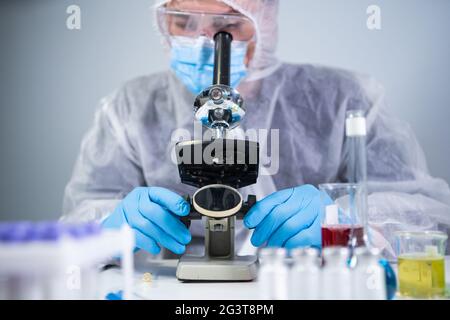 Scienziato che esamina il campione con un microscopio, facendo ricerca medica in laboratorio di scienza. Assistente di laboratorio maschile in Protect Foto Stock