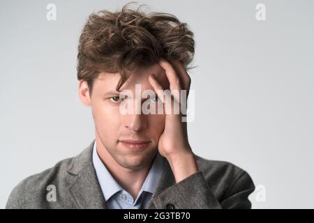 Giovane triste uomo pensieroso che ha mal di testa dopo il lavoro. Un giovane esausto che lavora molto e che tocca la testa, sta avendo un hea Foto Stock