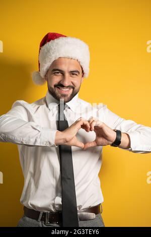 Bell'uomo sorridente bearded in cappello di Santa che mostra udire gesto isolato su sfondo giallo. Sorridente felice dipendente o gestire Foto Stock