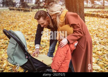 Una giovane famiglia cammina in un parco autunnale con un figlio e un neonato in passeggino. Famiglia all'aperto in un parco d'oro d'autunno Foto Stock