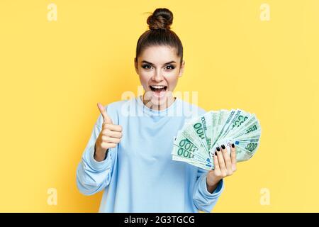 Felice giovane donna eccitato mostrando banconote di denaro con pollici in su Foto Stock