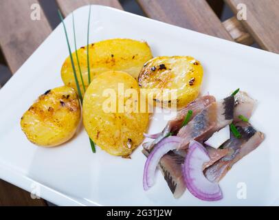 Patate fritte con fette di aringhe mite e cipolle servite sul piatto Foto Stock